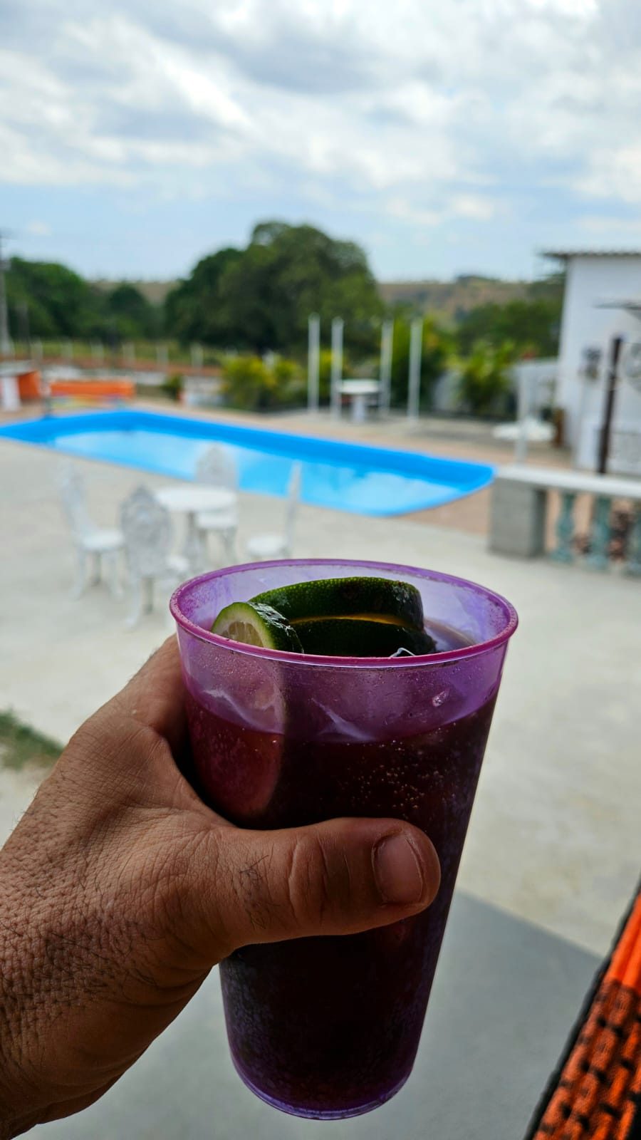 Drink gelado com rodelas de limão segurado em frente à piscina