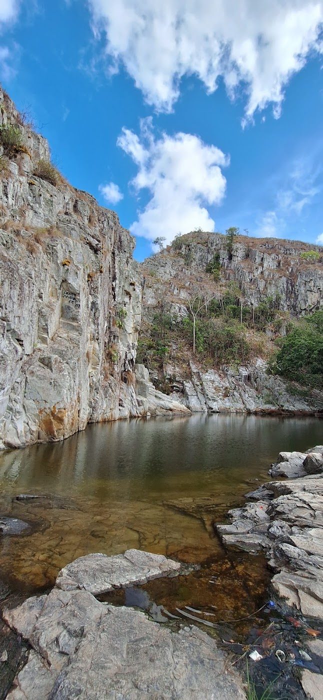 Lajedos de pedra e água rasa nas Poções da Ribeira sob céu azul